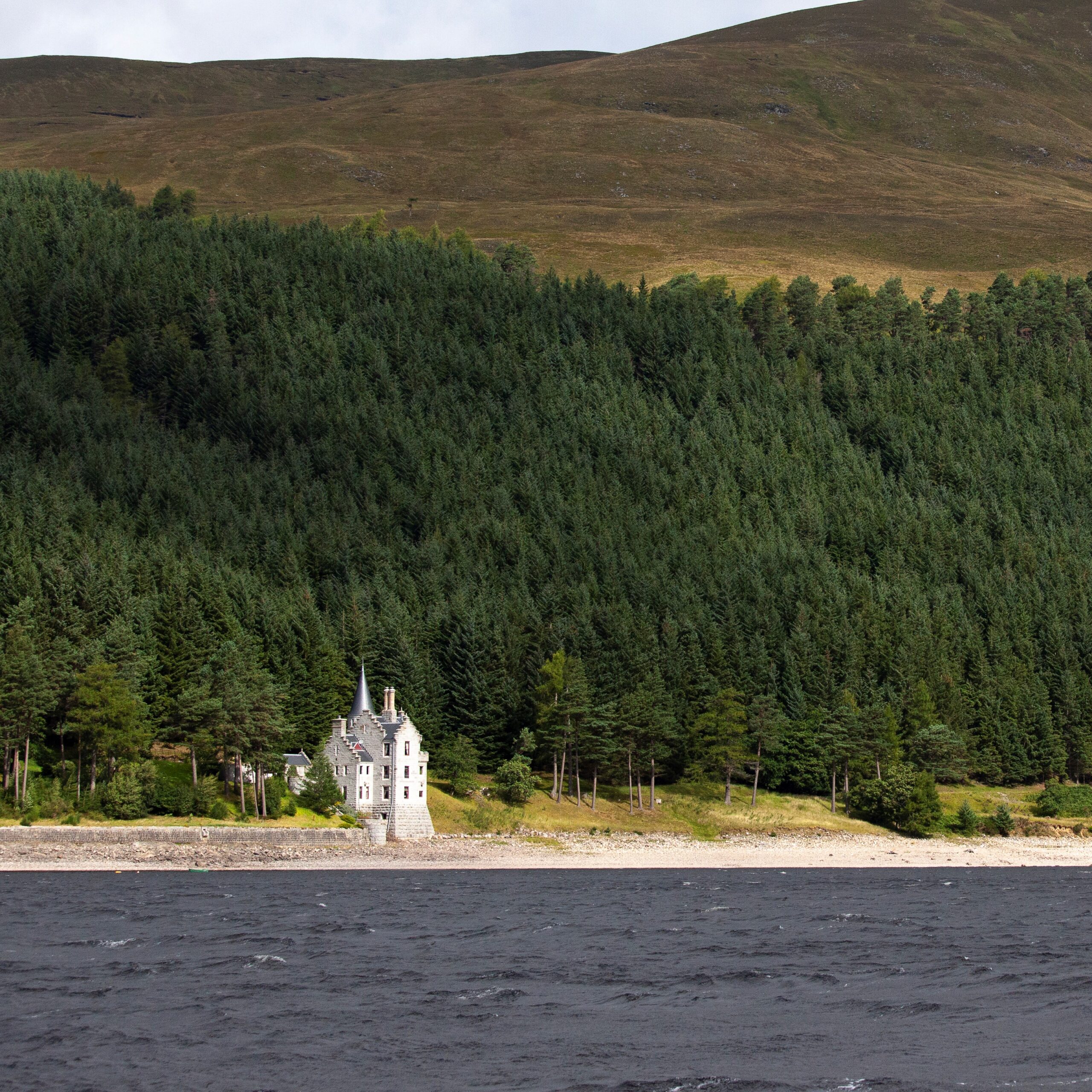 lodge-with-turret-at-edge-of-loch-and-forest-in-background